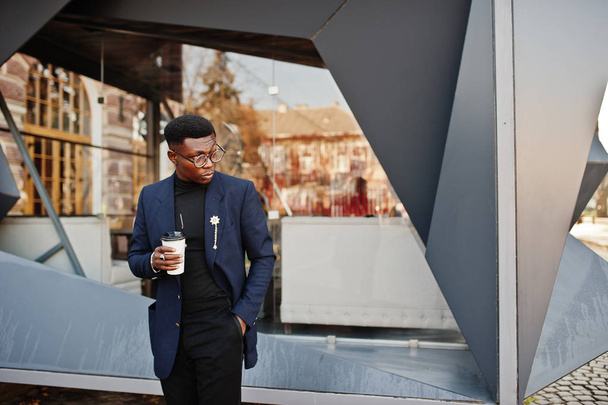 Amazingly looking african american man wear at blue blazer with brooch, black turtleneck and glasses posed at street. Fashionable black guy with cup of coffee. - Foto, Imagen