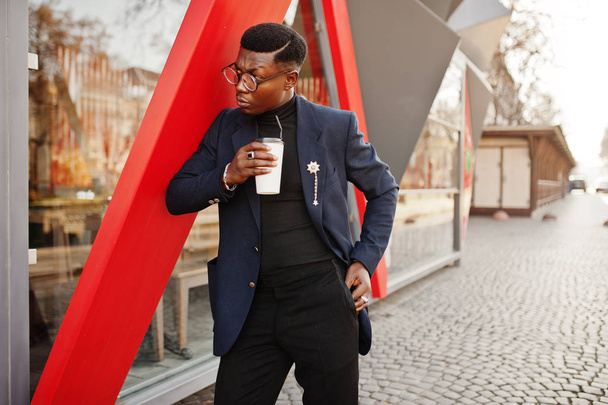 Amazingly looking african american man wear at blue blazer with brooch, black turtleneck and glasses posed at street. Fashionable black guy with cup of coffee. - Foto, Bild