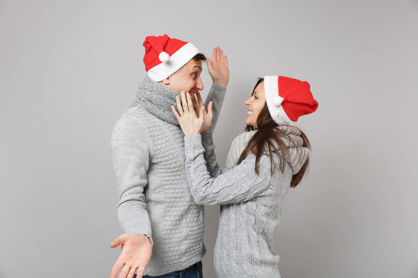 Merry διασκέδαση ζευγάρι άντρας κορίτσι με κόκκινο κασκόλ πουλόβερ γκρι καπέλο Santa Χριστούγεννα απομονώνονται σε φόντο γκρίζο τοίχο, στούντιο πορτρέτου. Ευτυχισμένο το νέο έτος 2019 γιορτή διακοπών κόμμα έννοια. Κοροϊδεύετε αντίγραφο χώρου - Φωτογραφία, εικόνα