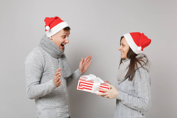 陽気な楽しいカップル女の子男赤灰色の壁の背景、スタジオ ポートレートに分離されたサンタのクリスマス ハット グレー セーター スカーフで。幸せな新しい年 2019年お祝いの休日党の概念。コピー スペースをモックアップします。 - 写真・画像