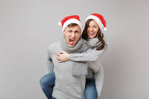 Feliz diversión pareja chica chico en rojo Santa Navidad sombrero suéteres grises bufandas aisladas en fondo de pared gris, retrato de estudio. Feliz Año Nuevo 2019 celebración fiesta concepto. Simular espacio de copia
 - Foto, imagen