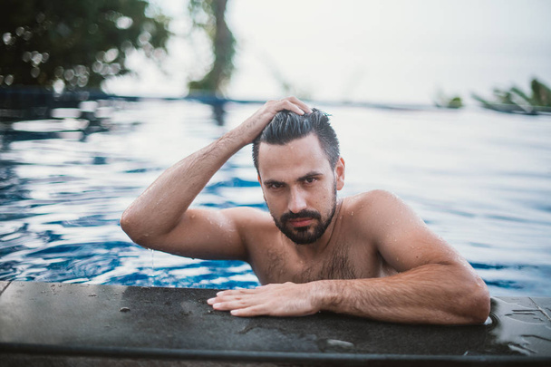 Portrait of a young handsome man in an outdoor pool. Attractive guy with a beard at the side of the pool - Φωτογραφία, εικόνα