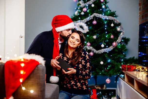 Ο σύζυγός στον Αϊ Βασίλη καπέλο έκπληξη τη γυναίκα του με ένα χριστουγεννιάτικο δώρο. Οικογενειακά Χριστούγεννα - Φωτογραφία, εικόνα