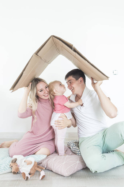 Smiling happy young mother and father standing in their living room at home with the cute baby girl in their arms. parents keep a roof over their heads. housing for a young family, mortgage - Фото, изображение