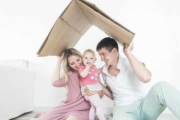 Smiling happy young mother and father standing in their living room at home with the cute baby girl in their arms. parents keep a roof over their heads. housing for a young family, mortgage - 写真・画像