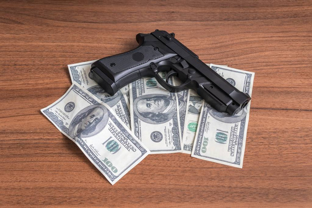 Robbery concept. Gun with money on wooden background. - Фото, изображение