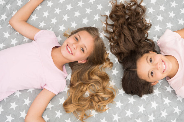 Children curly hairstyle relaxing. Keep hair curly even next morning. Girls children with long hair lay on bed top view. Conditioner mask organic oil keep hair shiny and healthy. Amazing hair tips - Fotó, kép
