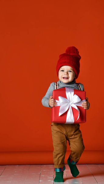 Portrait of a little boy  with a pompon. holding a large gift box with a white bow.  - Foto, Imagem