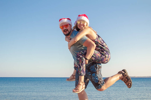 mies reppuselässä tyttöystävänsä joulun hatut ja aurinkolasit rannalla meren
 - Valokuva, kuva