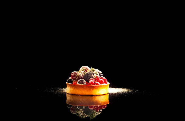 Cupcake en bessen met reflectie op zwarte achtergrond, close-up, kopieerruimte   - Foto, afbeelding