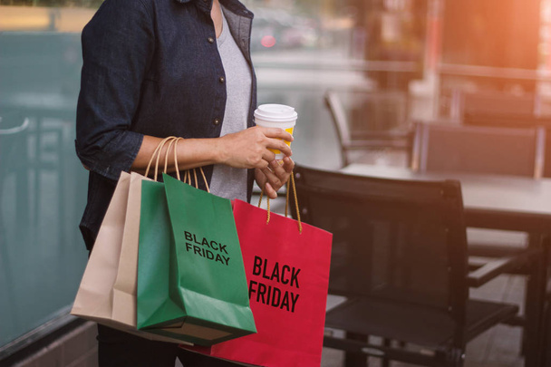 Viernes Negro, Mujeres con taza de café en la mano sosteniendo bolsas de compras mientras camina sobre el fondo del centro comercial
. - Foto, imagen