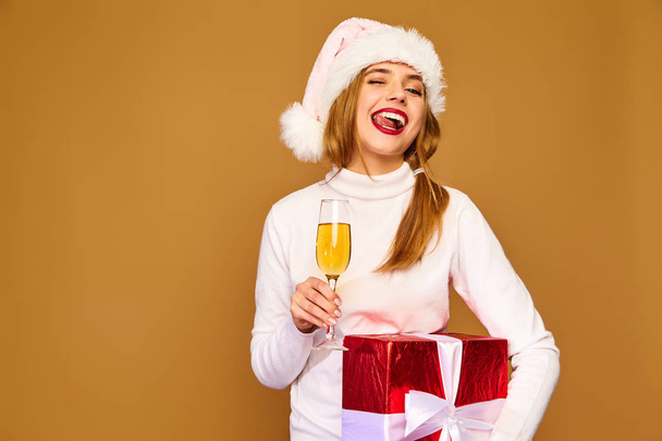 Christmas,x-mas, concept. Smiling beautiful woman in white winter sweater.Girl posing on golden background.Model with big gift box drinking champagne.Having fun, celebrating New Year - Foto, afbeelding