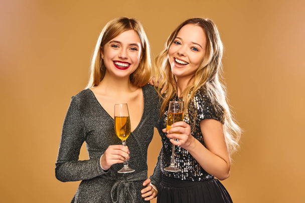Όμορφη ξανθιά γυναίκες γιορτάζει το νέο Year.Models να διασκεδάζουν στο πάρτι μόδας. Ευτυχισμένος χαμογελαστά κορίτσια στο κομψό λαμπερό φορέματα με ποτήρια σαμπάνια. Απομονωμένα σε χρυσό υπόβαθρο - Φωτογραφία, εικόνα