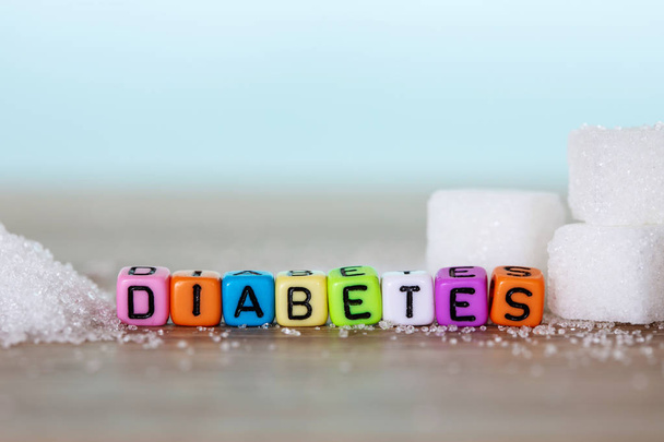 weißer Zuckerwürfel und bunter Buchstabenblock mit Diabetes-Wort auf Holztisch mit hellblauem Hintergrund, ungesundes Süßkost-Konzept für die Kampagne zum Welt-Diabetes-Tag am 14. November - Foto, Bild