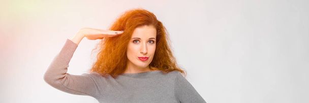 Charming young girl with red hair. A young girl in a gray sweater. Young girl on a gray background. A young girl put her hand to her head. - Photo, Image