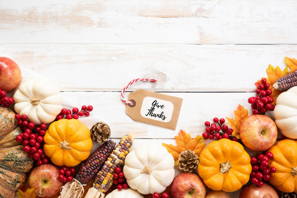 Vista superior de las hojas de arce de otoño con calabaza y bayas rojas sobre fondo de madera blanca. Concepto del día de Acción de Gracias
. - Foto, imagen