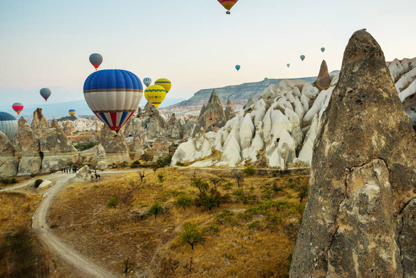 Many colorful hot air balloons flight above mountains - panorama of Cappadocia at sunrise. Wide landscape of Goreme valley in Cappadocia - billboard background for your travel concept in Turkey. - Φωτογραφία, εικόνα