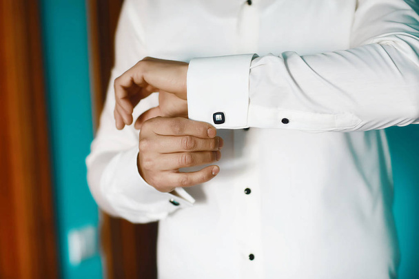 Γαμπροί πρωινό προετοιμασία, όμορφος γαμπρός να πάρει ντυμένος και προετοιμασία για το γάμο, ο γαμπρός φοράει μανικετόκουμπα σε ένα λευκό πουκάμισο. - Φωτογραφία, εικόνα