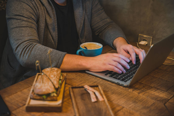 Mies tekee läppäriä kahvilassa syöden voileipää ja juoden kahvia. elämäntapa käsite
 - Valokuva, kuva