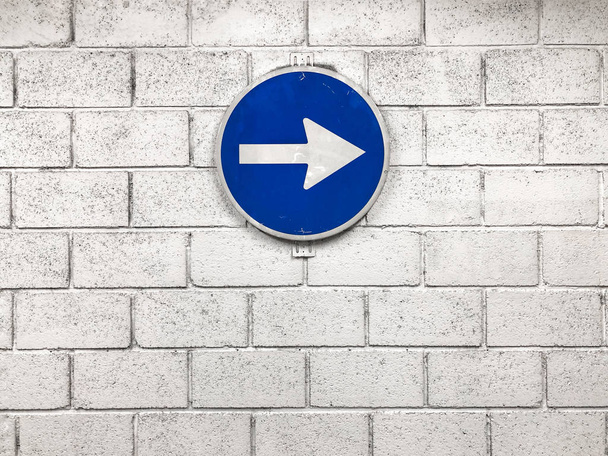 белая стрелка на синем дорожном знаке, висящем на стене и указывающем правильное направление
 - Фото, изображение