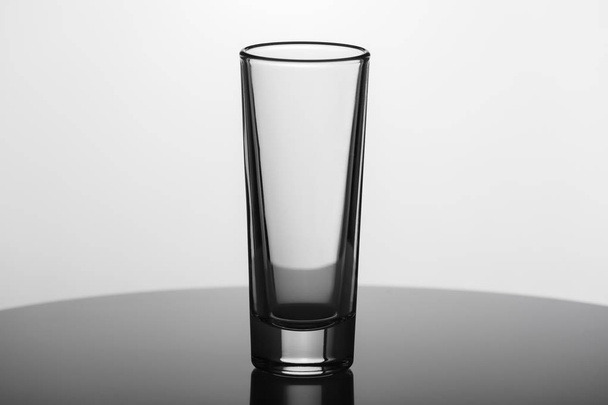 Pustej szklanki dla wódki na powierzchni odbijającej na białym tle. Dania dla alkoholu - Zdjęcie, obraz