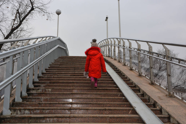 Giovane ragazza in giacca rossa sollevare sulle scale
. - Foto, immagini