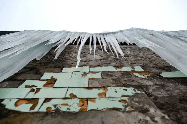 icles appeso al tetto del vecchio edificio in mattoni con cubi di piastrelle antiche, ghiaccio traumatico acre, disgelo all'inizio della primavera, guardare dal basso, insieme. - Foto, immagini