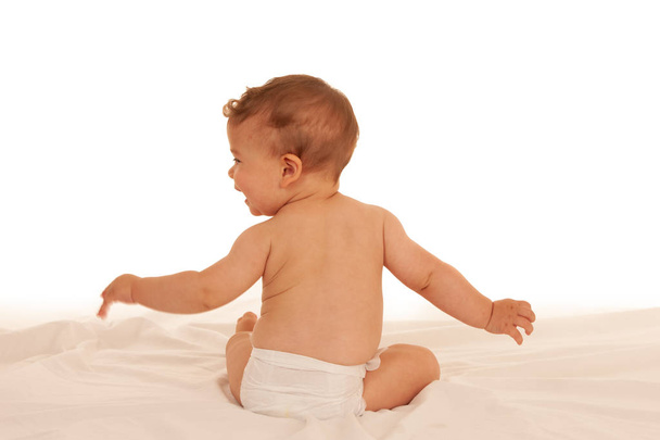 Turned away baby plays on bed isolated over white background - Fotoğraf, Görsel