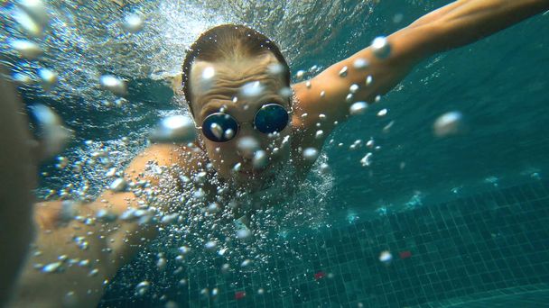 Un jeune homme blanc beau faisant un selfie sous-marin sur une caméra d'action. Portrait d'un jeune homme avec des lunettes se prenant à la caméra sous l'eau
. - Photo, image