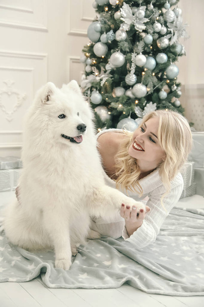 beautiful blonde in white clothes with a white husky on the background of Christmas tree - Fotoğraf, Görsel