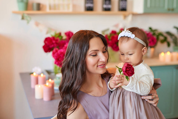 mom and daughter in elegant dresses in the kitchen, decorated with peonies - Photo, Image