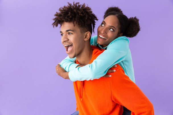 Photo of pleased african american man piggybacking his teenage sister isolated over violet background - Фото, зображення