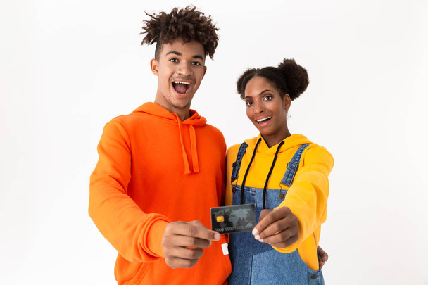 Image of happy african american couple in colorful clothes smiling and holding credit card together isolated over white background - 写真・画像