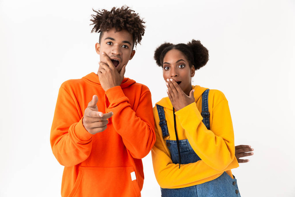 Image of excited african american couple in colorful clothes pointing finger at you isolated over white background - Foto, Bild