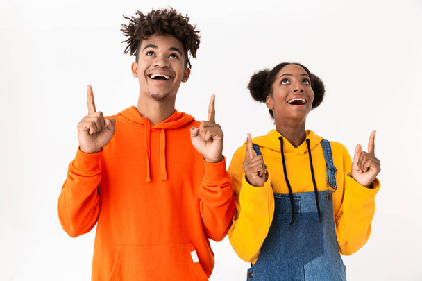 Image of african american couple in colorful clothes pointing fingers upward at copyspace isolated over white background - Photo, image