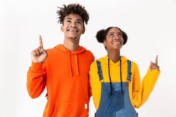 Image of african american man and woman in colorful clothes pointing fingers upward at copyspace isolated over white background - Fotografie, Obrázek
