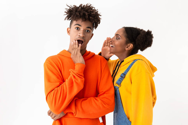 Photo of young african american woman talking secrets in ear of her brother isolated over white background - Foto, Imagem