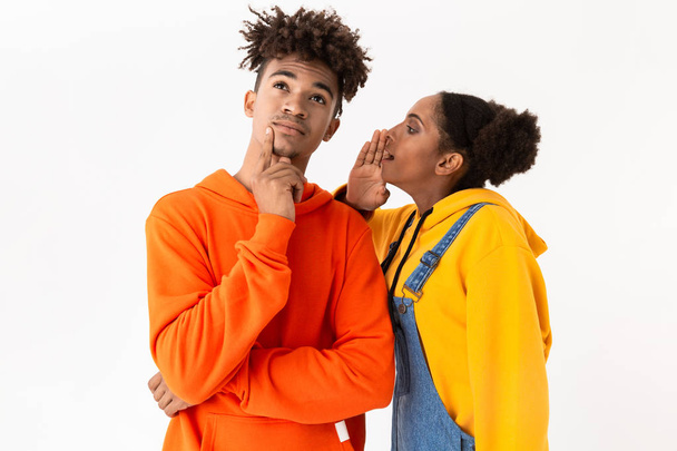 Photo of african american woman talking secrets in ear of her boyfriend isolated over white background - Fotó, kép