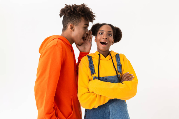 Photo of handsome african american man talking secrets in ear of his girlfriend isolated over white background - Foto, Imagem