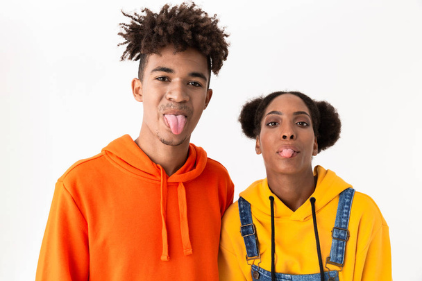 Image of amusing african american couple in colorful clothes having fun and showing tongue at camera isolated over white background - Foto, afbeelding