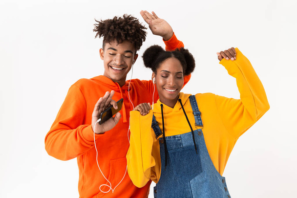 Photo of young african american couple in colorful clothes dancing while listening to music together with earphones isolated over white background - Fotografie, Obrázek