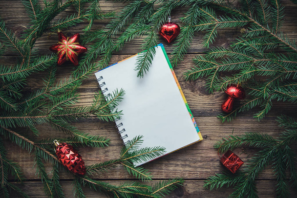 Tinted Christmas picture with a notebook, fir branches, red toys on a wooden rustic background, copy space, top view - Foto, Bild