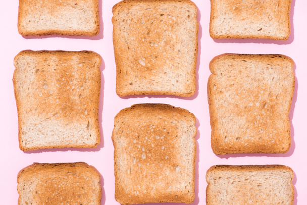 top view of repetitive pattern of crispy toasts on pink surface - Fotó, kép