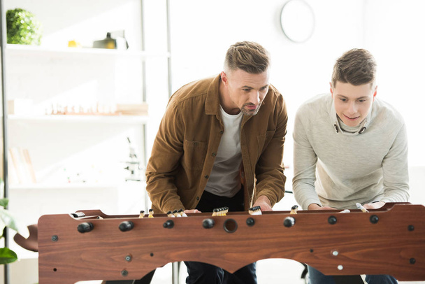 father and teen son playing table football at home during sunny day - Фото, зображення