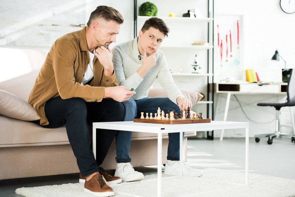 Nachdenklicher Vater und Teenager-Sohn spielen zu Hause Schach - Foto, Bild