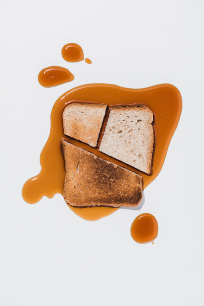 κάτοψη του φέτα ψωμί με ψημένα κομμάτια στο χυμένο καφέ σιρόπι σε λευκή επιφάνεια - Φωτογραφία, εικόνα