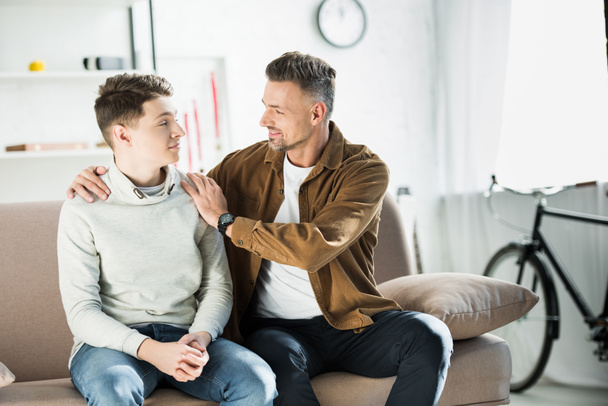 father hugging teen son on sofa at home - Foto, Bild