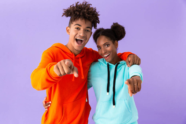 Photo of joyful african american brother and sister standing together and pointing finger at camera isolated over violet background - Valokuva, kuva