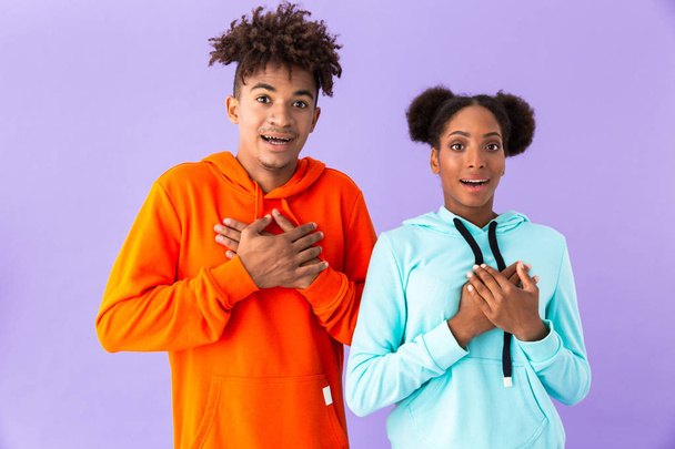 Photo of teenage african american couple standing together with hands at hearts isolated over violet background - Foto, immagini