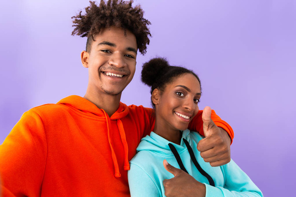 Photo of joyful african american brother and sister standing together and showing thumbs up isolated over violet background - 写真・画像
